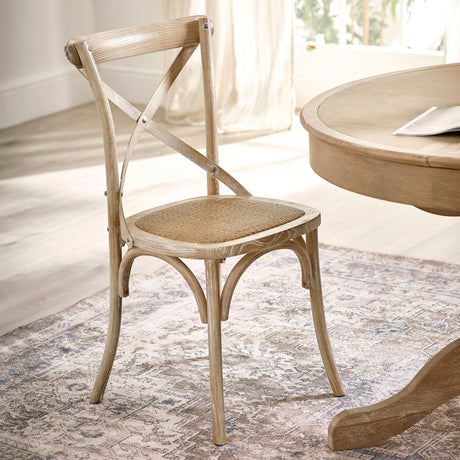 Light wooden dining chair with cane seat angled in bright room near round wooden table