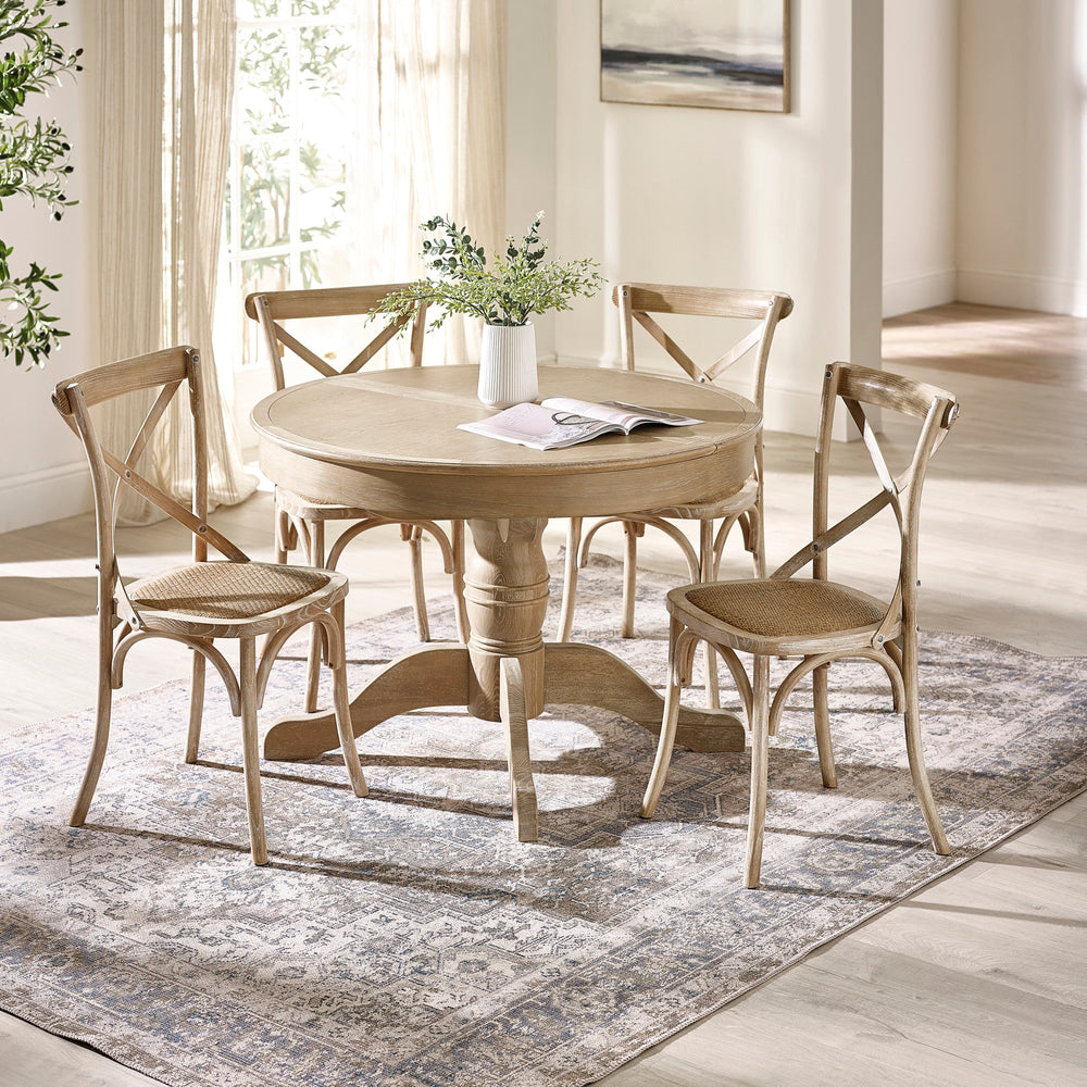 Set of four light wood dining chairs around round dining table in bright room with rug and vase on table