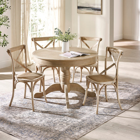 Set of four light wood dining chairs around round dining table in bright room with rug and vase on table