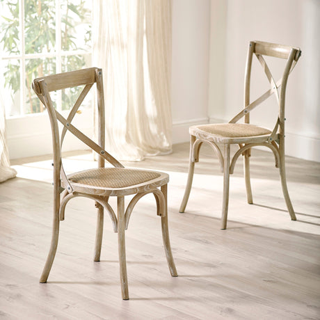 Two light wooden dining chairs with cane seats angled in sunlit room with sheer curtains