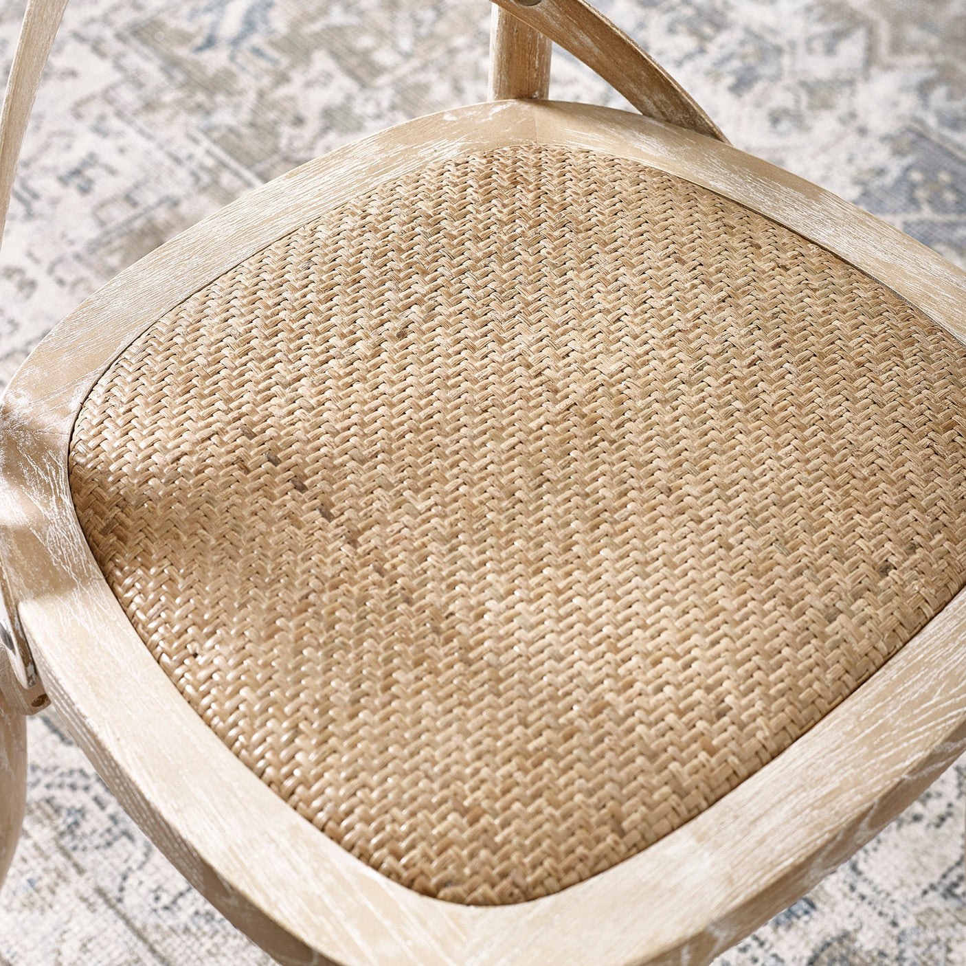Close view of cane seat with woven pattern framed in light wood with whitewashed finish