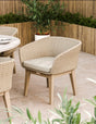 Beige woven outdoor dining chair with cushion on tiled patio, wooden planter in background
