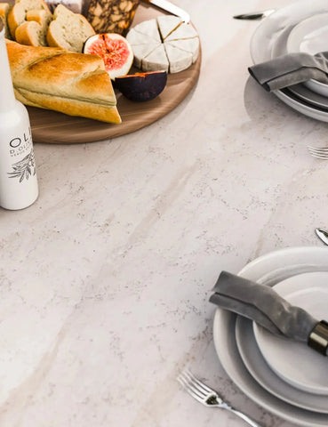 white marble dining table set with plates, cutlery, grey napkin, bread and cheese platter