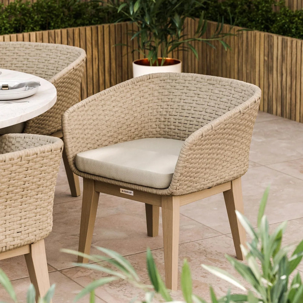 Woven rattan dining chair with beige cushion beside round table on patio
