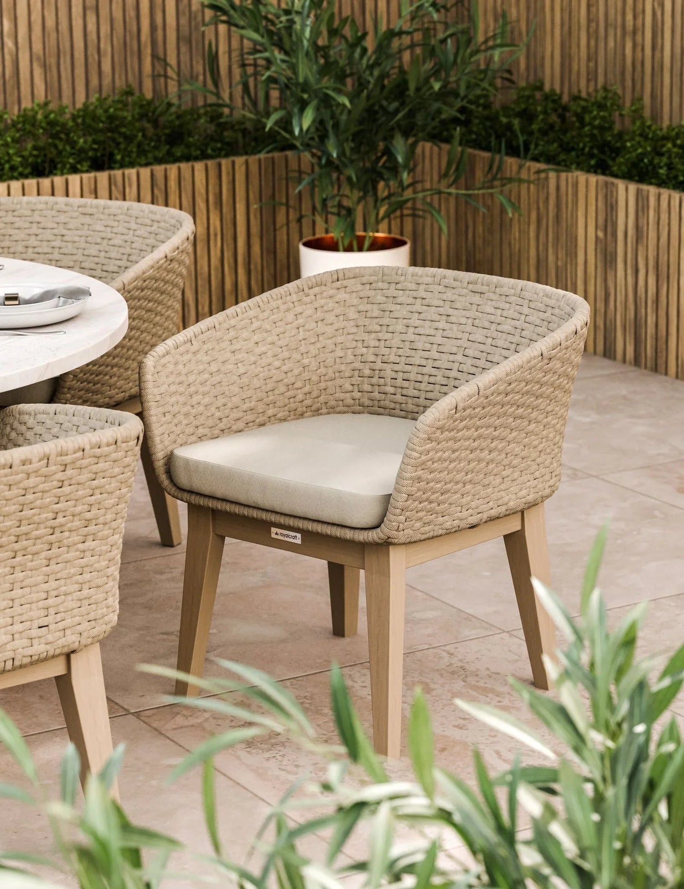 Woven rattan dining chair with beige cushion beside round table on patio