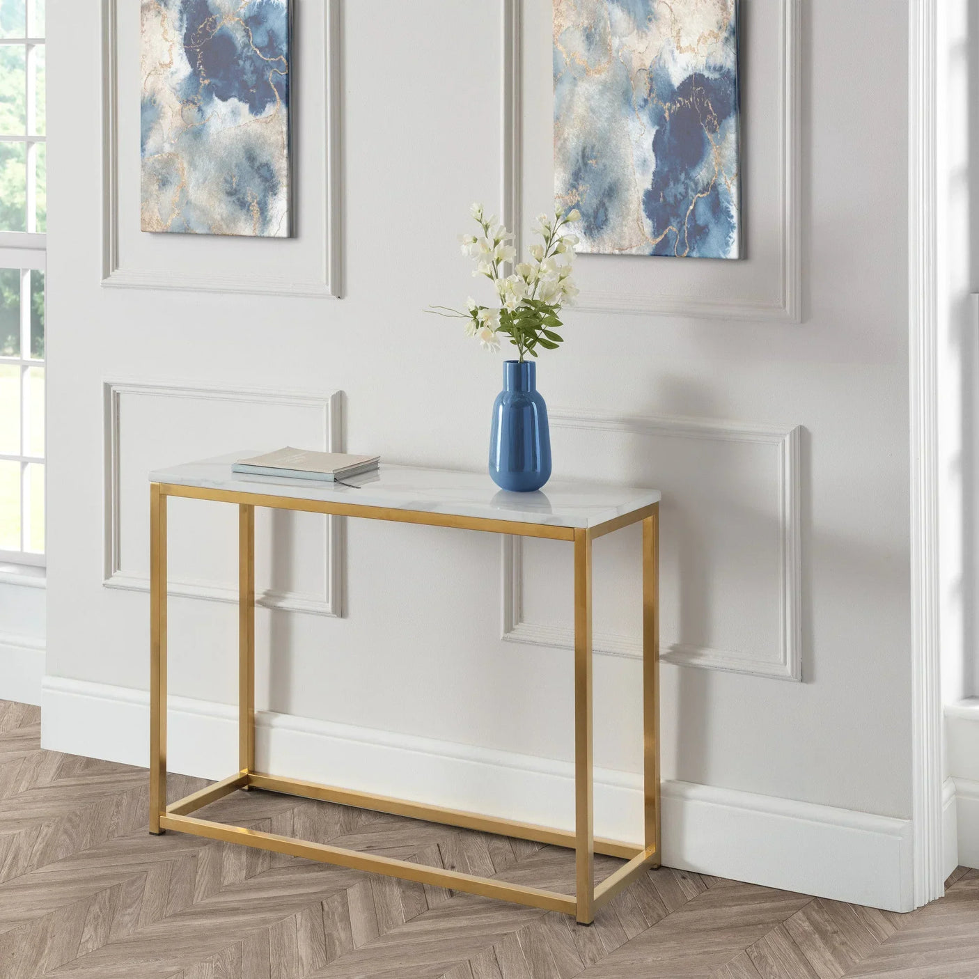 Marble top console table with gold metal frame, blue vase and book in modern hallway