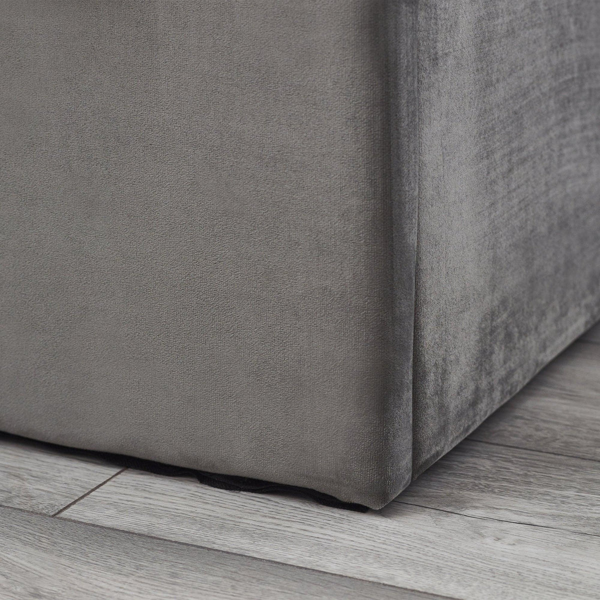 Grey upholstered storage bed corner detail on wood floor