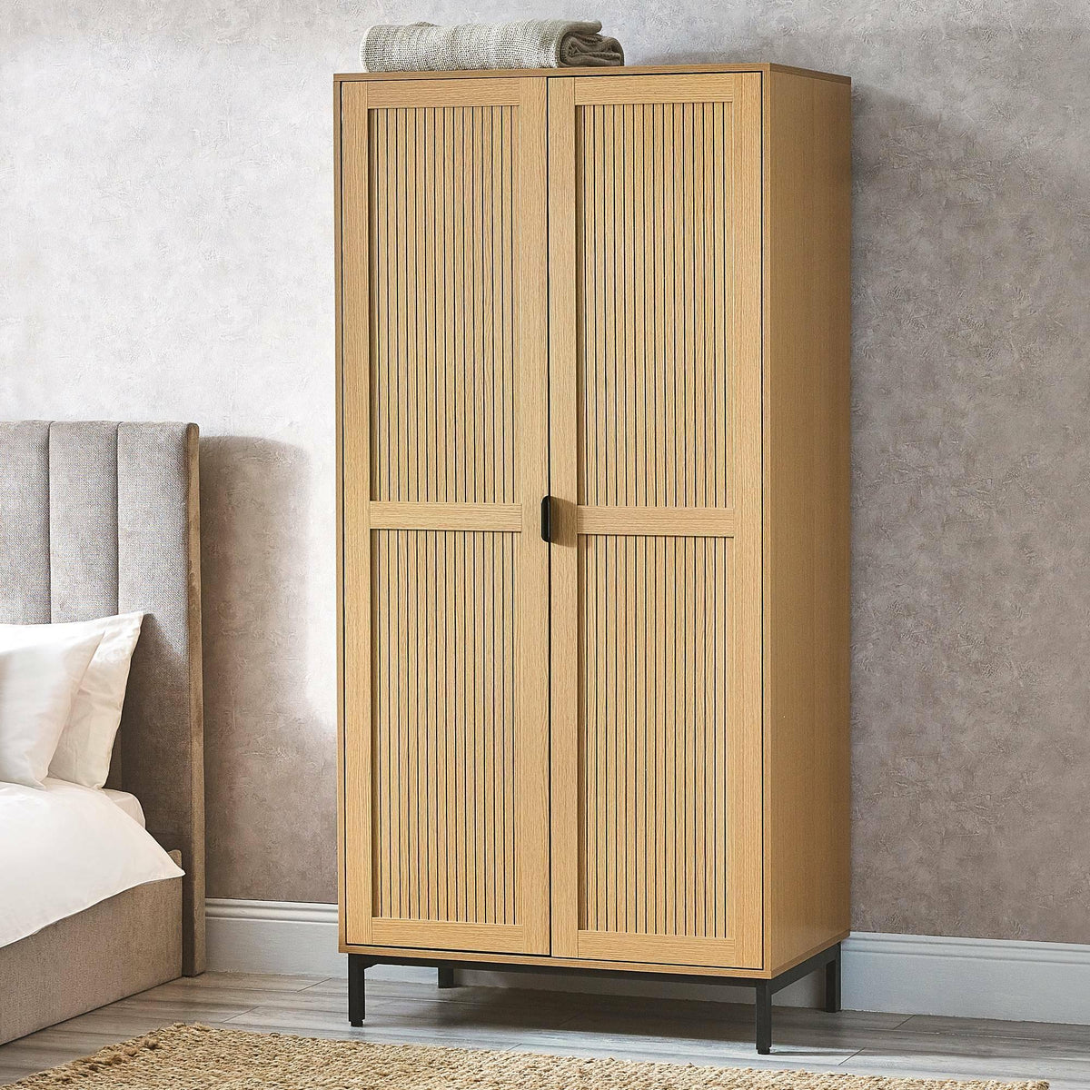 Oak effect 2 door wardrobe with black legs beside upholstered bed in modern bedroom