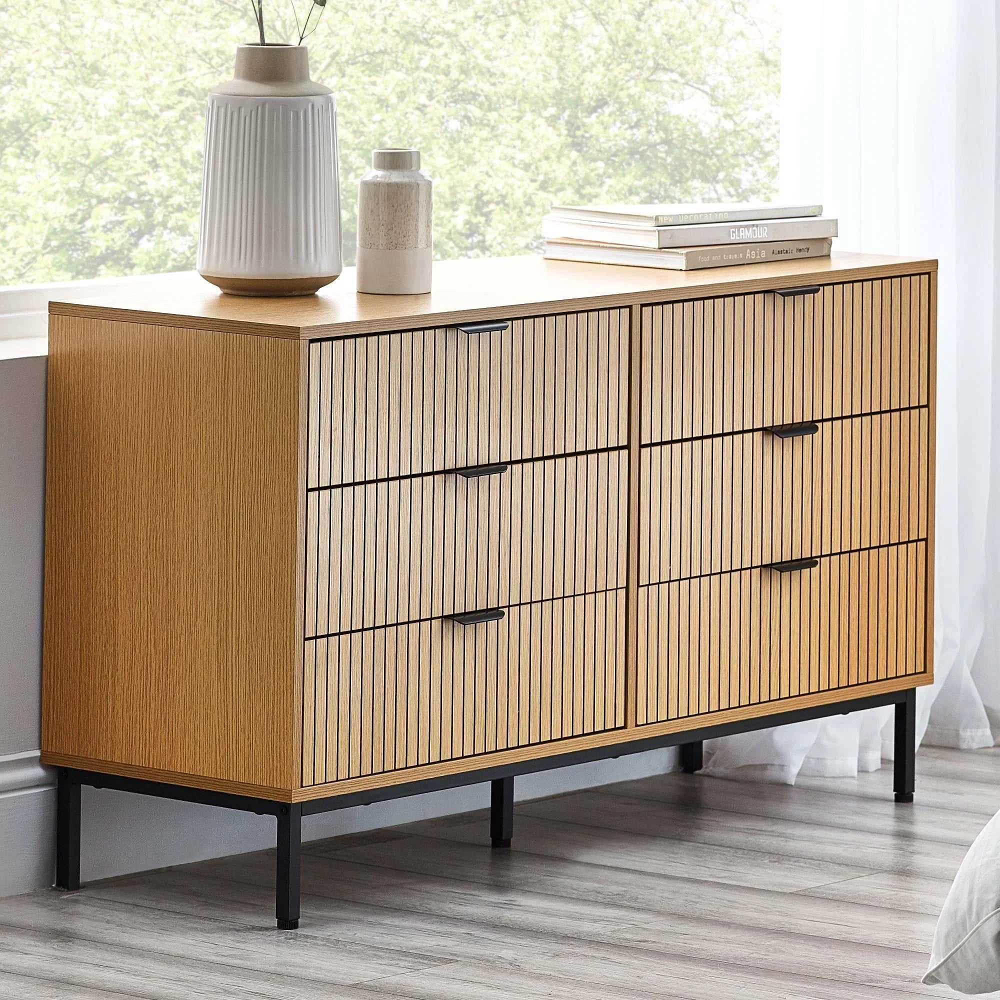 Light oak chest of drawers with vertical slat design and black legs in modern bedroom