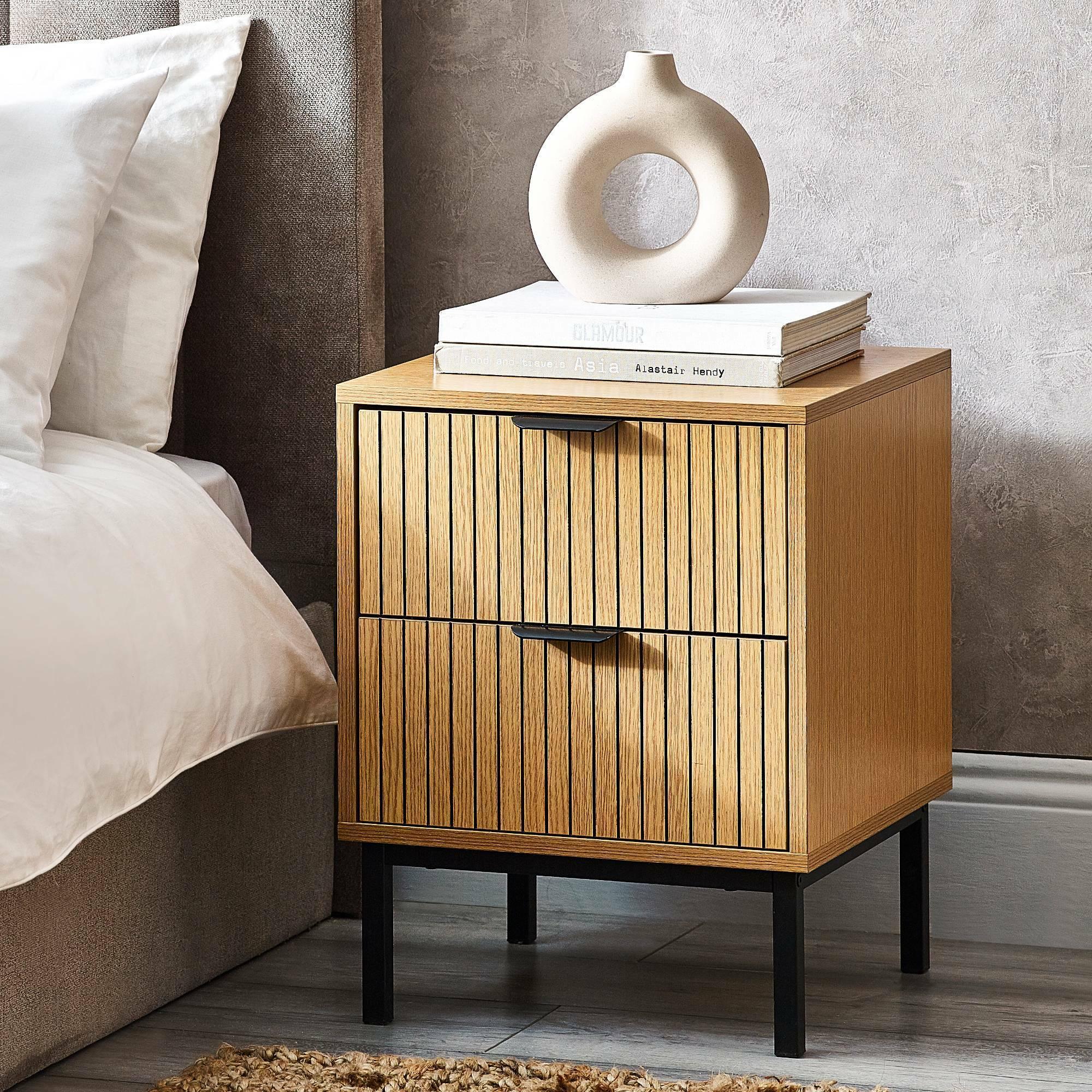 Sia 2 drawer bedside table with wood grain finish and black handles beside a bed