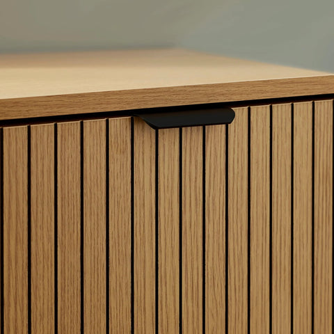 Oak slatted cabinet door with vertical grooves and black handle, close-up view