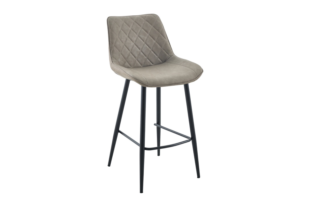 A modern bar stool with a light taupe-gray quilted velvet upholstered seat and backrest, supported by slim black metal legs.