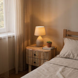 Nursery room with wooden nightstand, lamp, and books near a window.