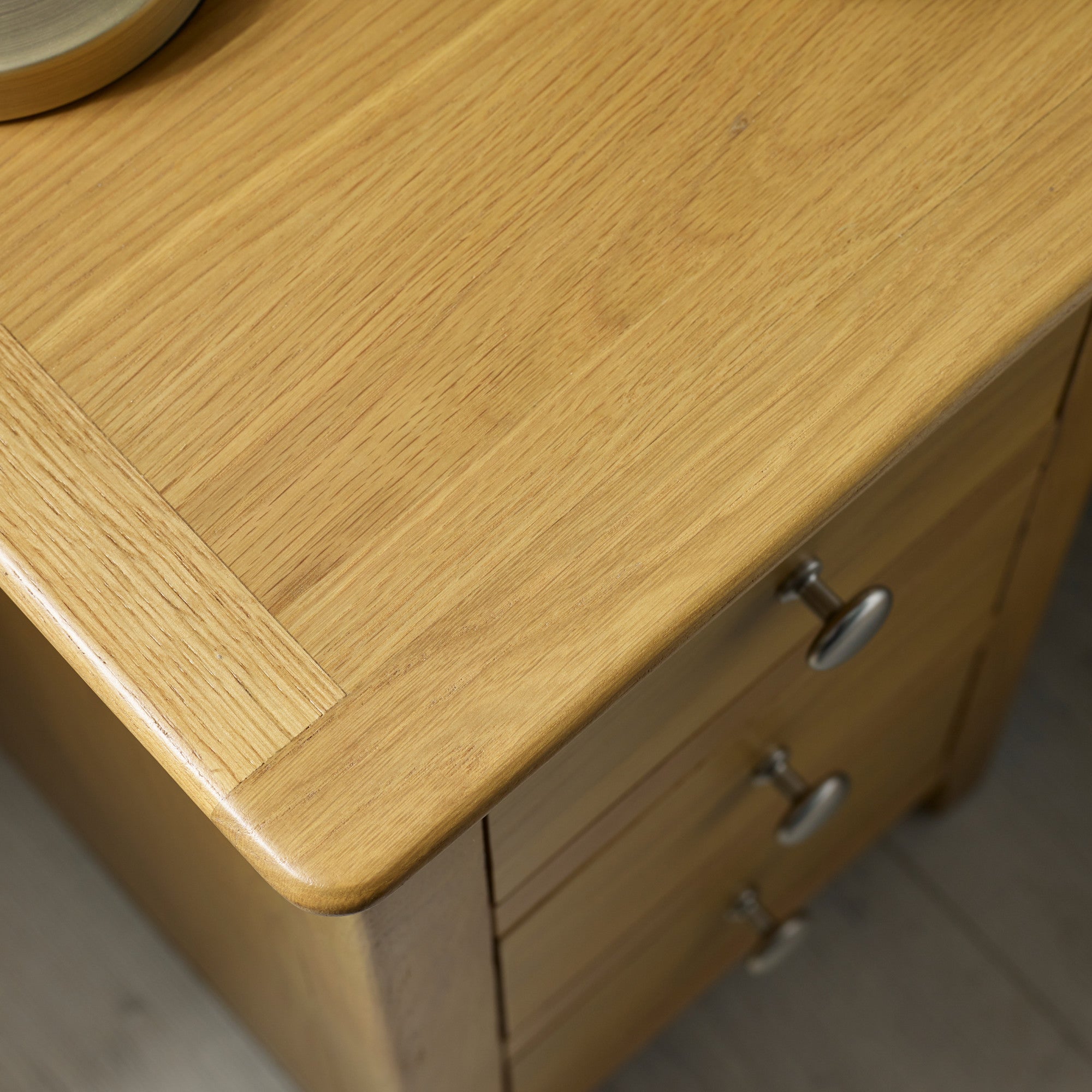 Close-up of light oak tabletop with smooth edges and metal drawer knobs on wooden furniture