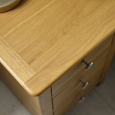 Close-up of light oak tabletop with smooth edges and metal drawer knobs on wooden furniture