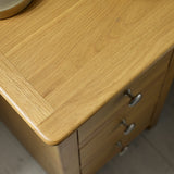 Close-up of light oak tabletop with smooth edges and metal drawer knobs on wooden furniture