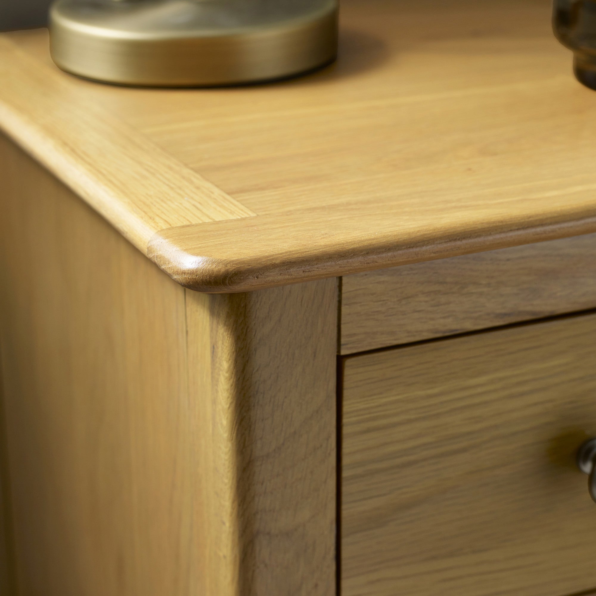 Close-up of round silver drawer knob on light oak bedside table with wood grain visible