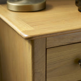 Close-up of round silver drawer knob on light oak bedside table with wood grain visible
