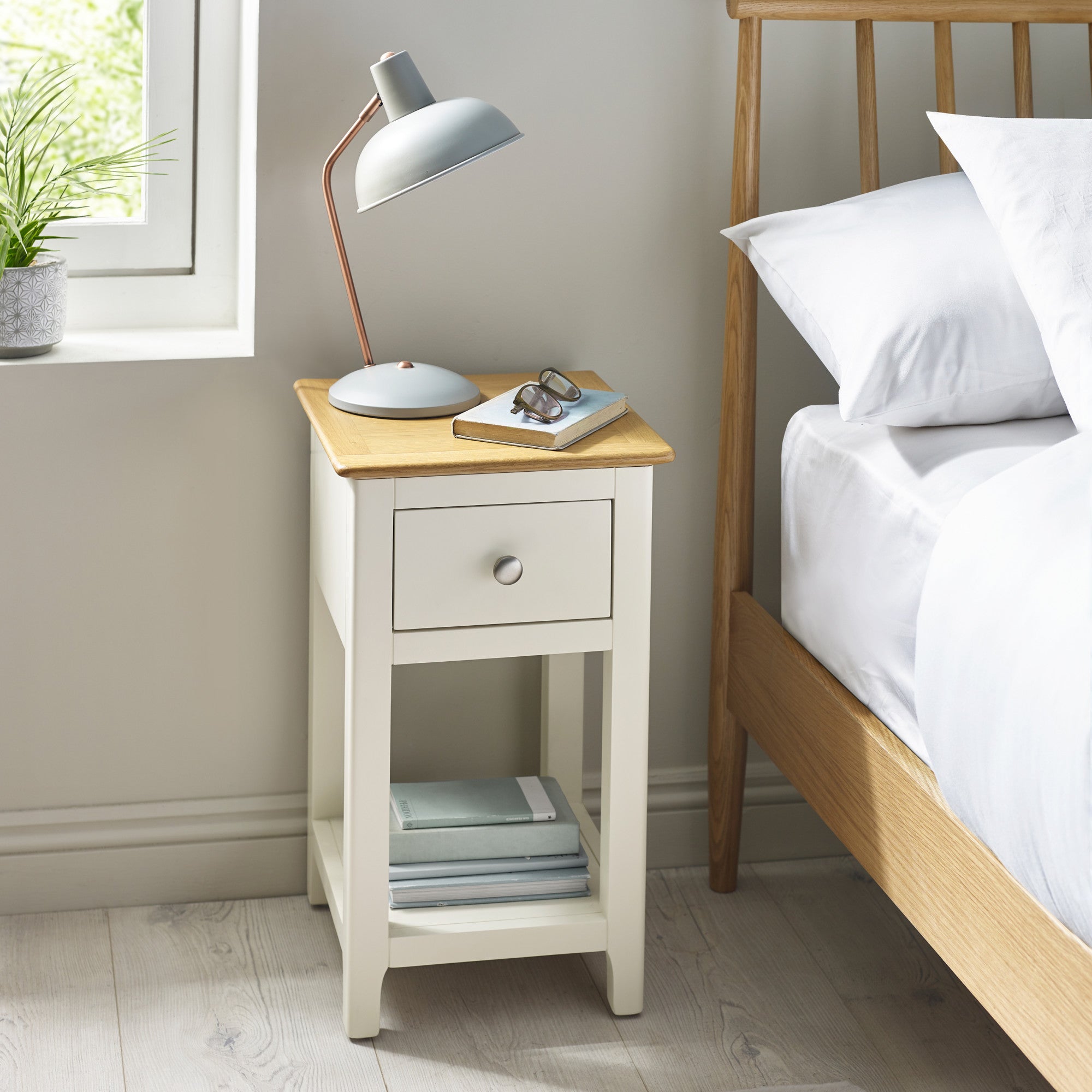 Cream painted bedside table with oak tabletop, closed drawer, lamp, and book beside bed