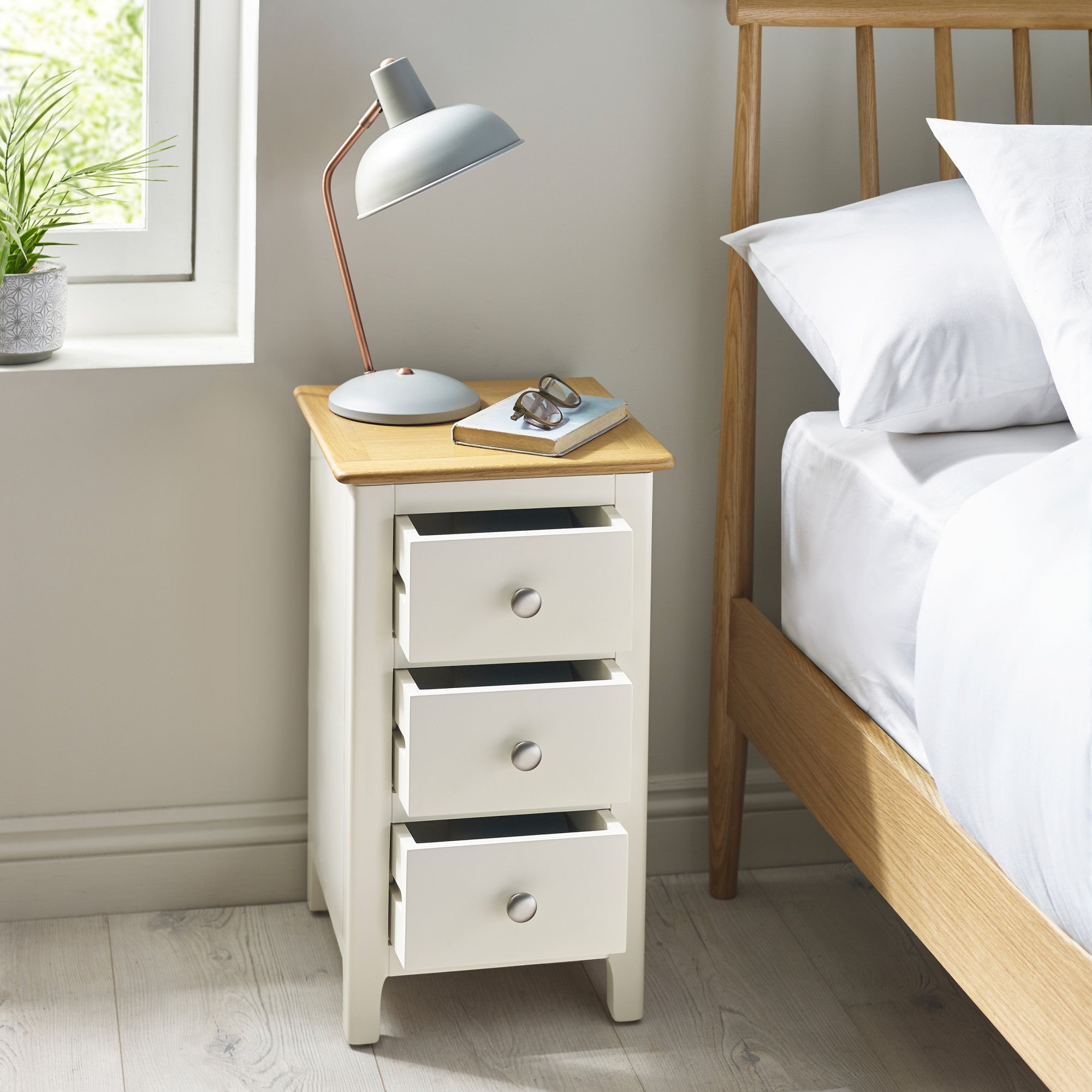 Cream colored 3 drawer bedside next to wooden bed, all three drawers pulled open