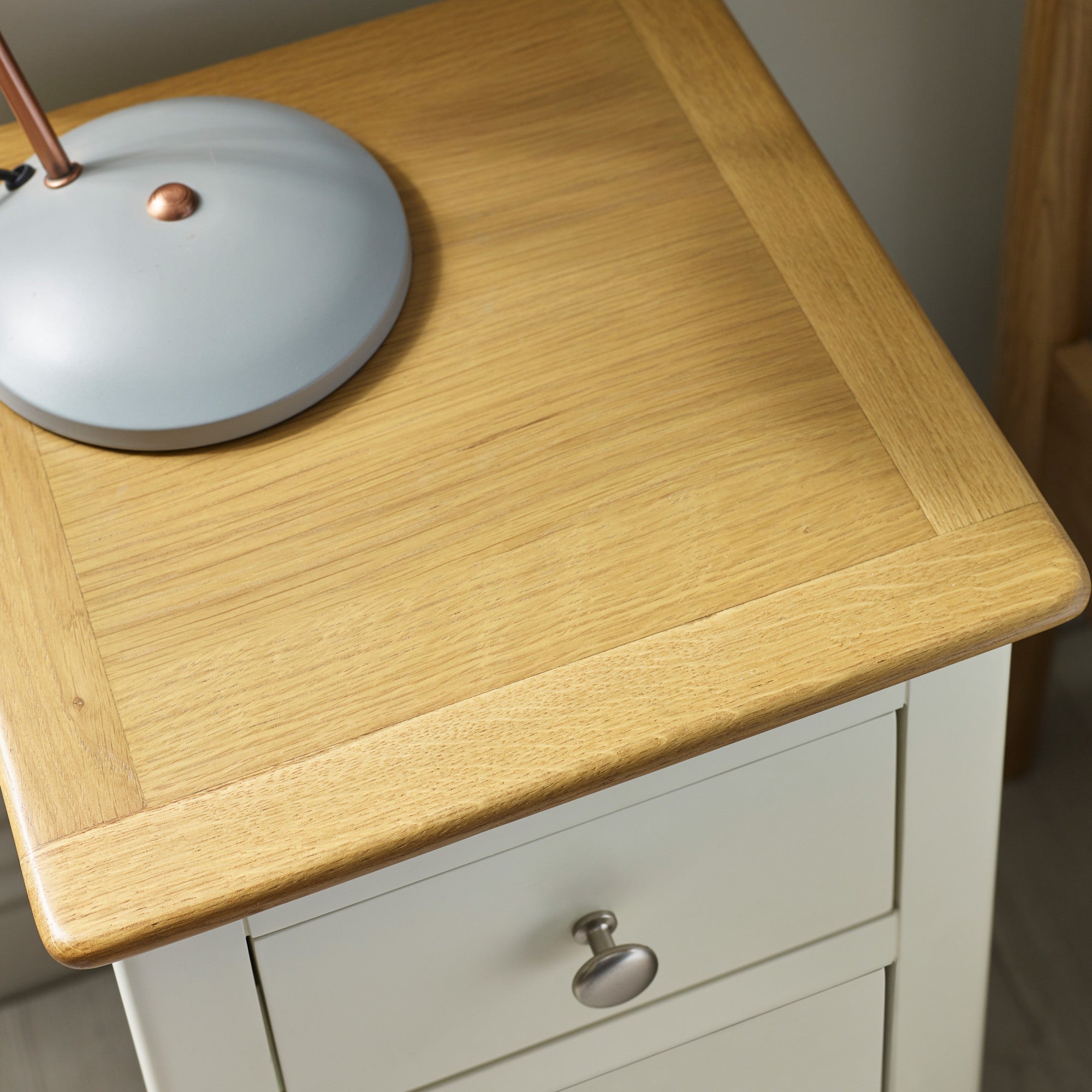 Close-up of natural oak top with wood grain and beige drawer front with round metal knob