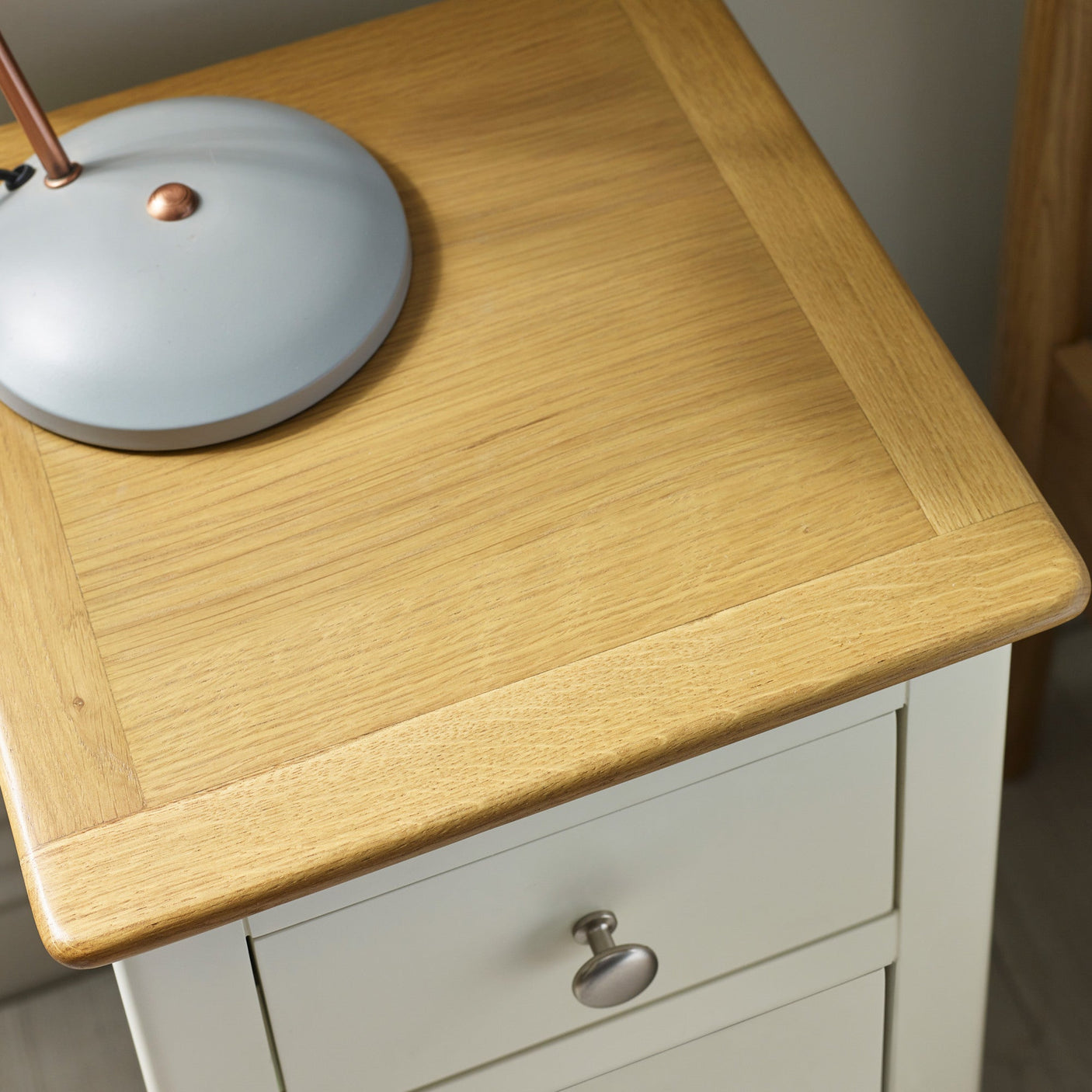 Close-up of natural oak top with wood grain and beige drawer front with round metal knob