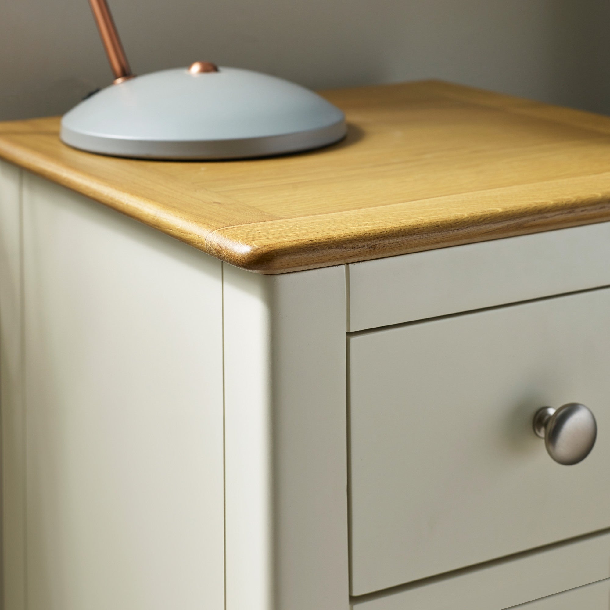 Close-up of bedside top with natural oak wood finish, beige body, and grey lamp base on corner