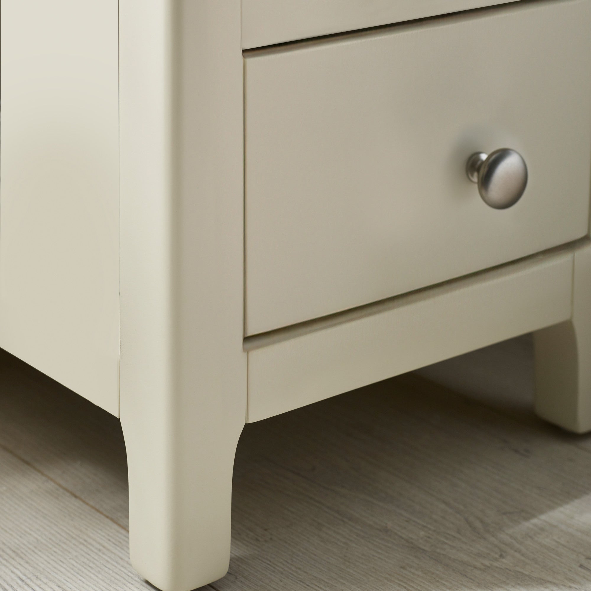 Close-up of beige bedside leg with rounded edges and metal drawer knob on light wooden floor