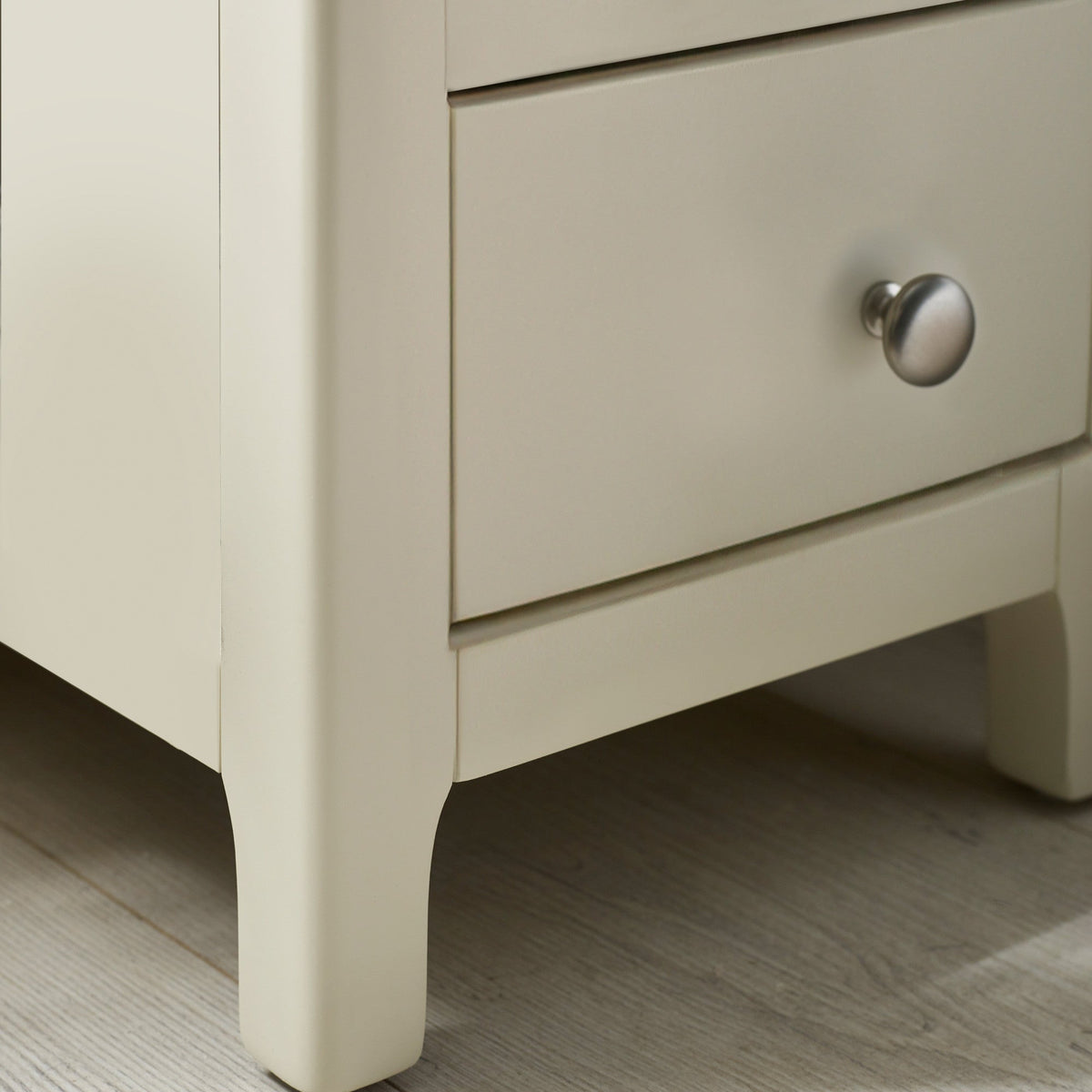 Close-up of beige bedside leg with rounded edges and metal drawer knob on light wooden floor