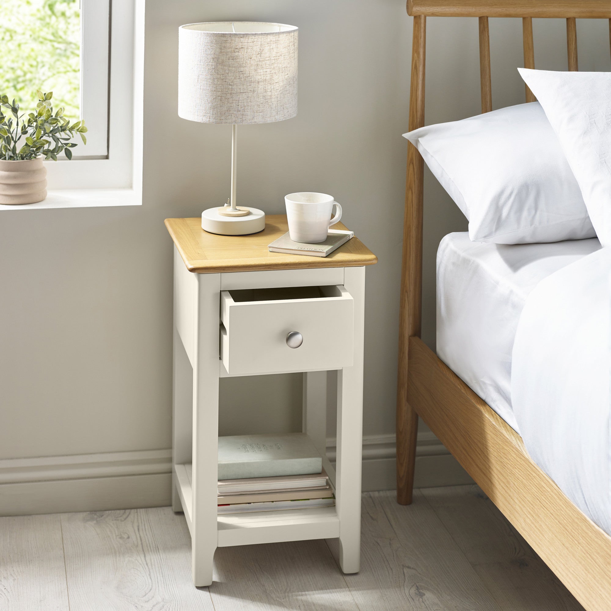 Bedside table with open drawer showing storage inside next to a bed with white bedding