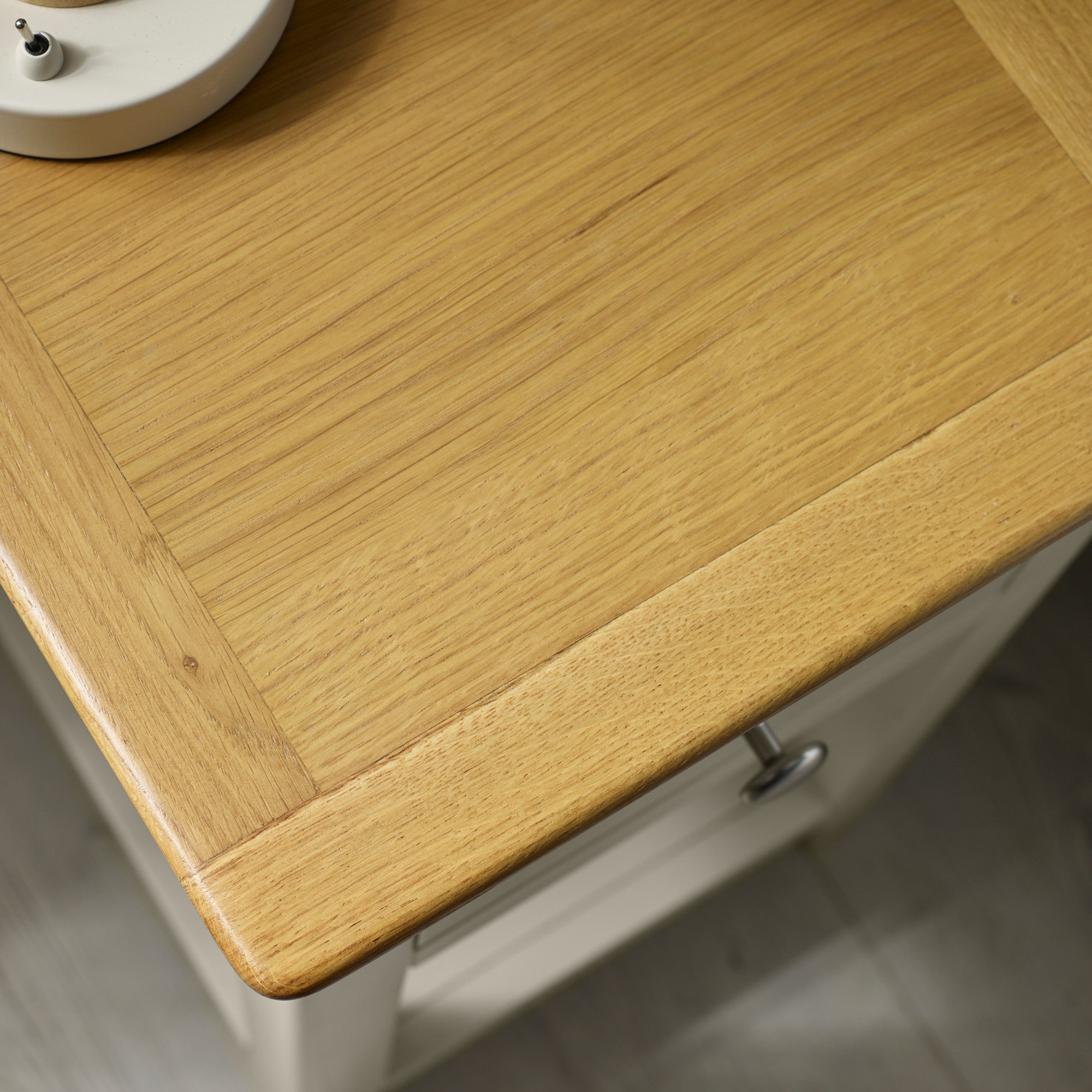Close-up of oak wood tabletop grain showing texture and round metal drawer knob on pale grey bedside table.