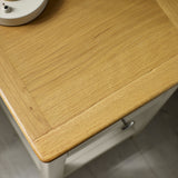 Close-up of oak wood tabletop grain showing texture and round metal drawer knob on pale grey bedside table.