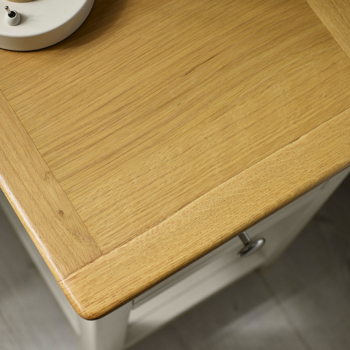 Close-up of oak wood tabletop grain showing texture and round metal drawer knob on pale grey bedside table.