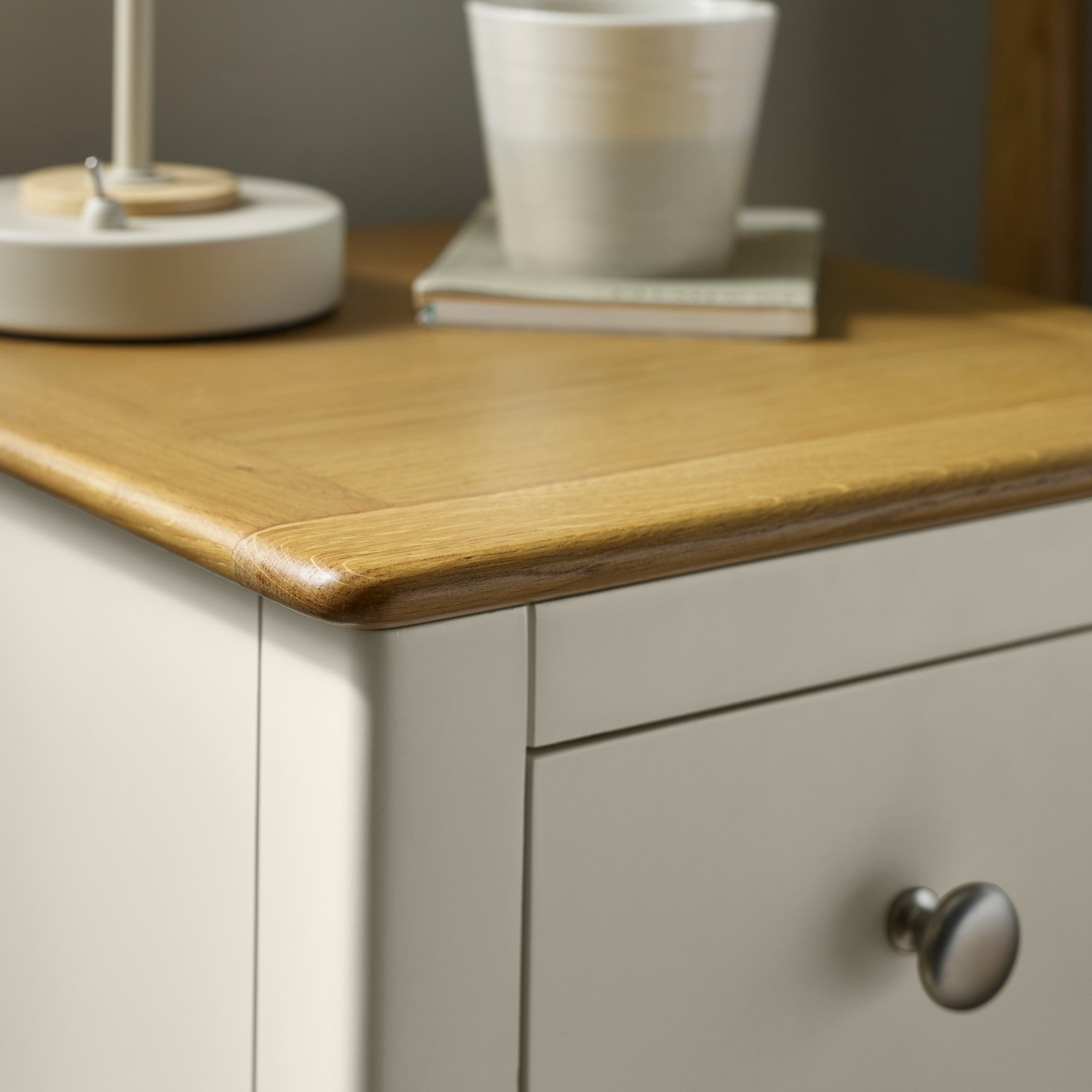Close view of natural wood bedside table top showing smooth rounded edge with cup and books placed on top
