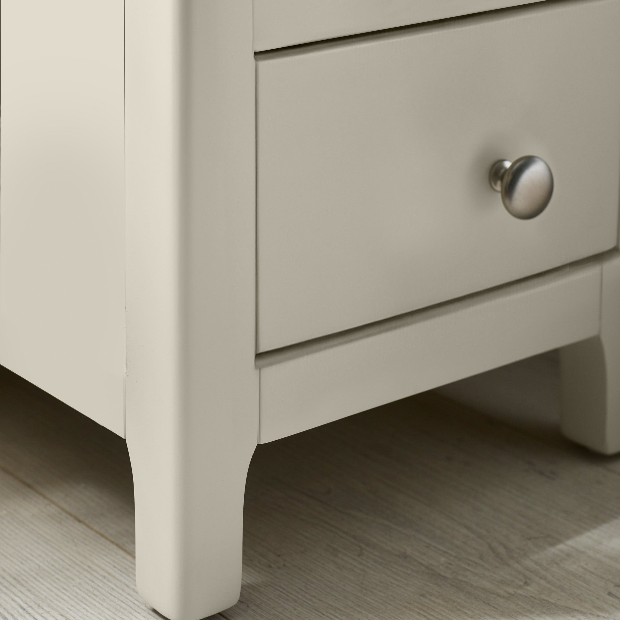 Close-up of bedside leg detailing painted light grey with gentle curve near base on wooden flooring