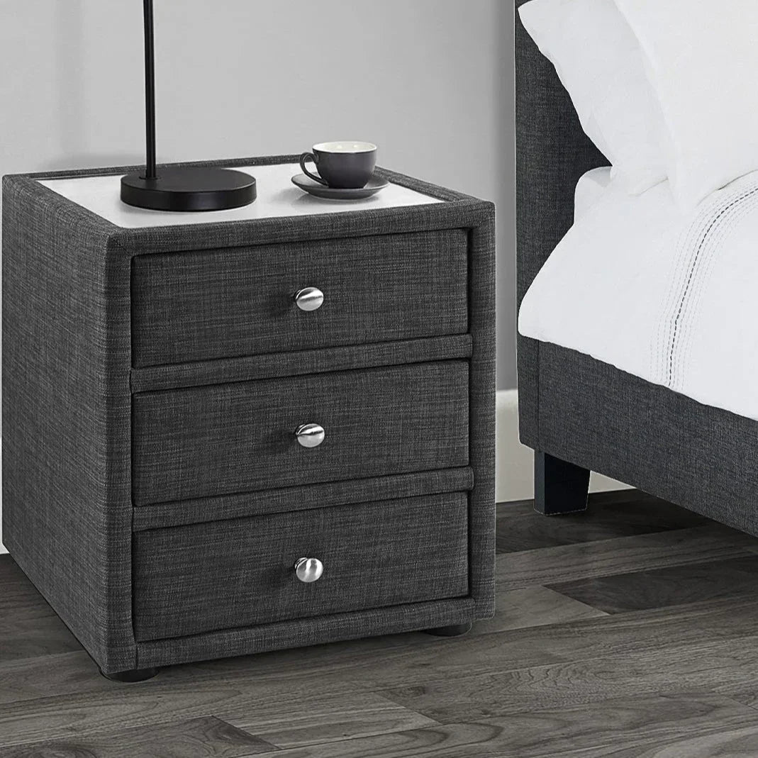 Slate linen 3 drawer bedside table with chrome handles next to upholstered bed