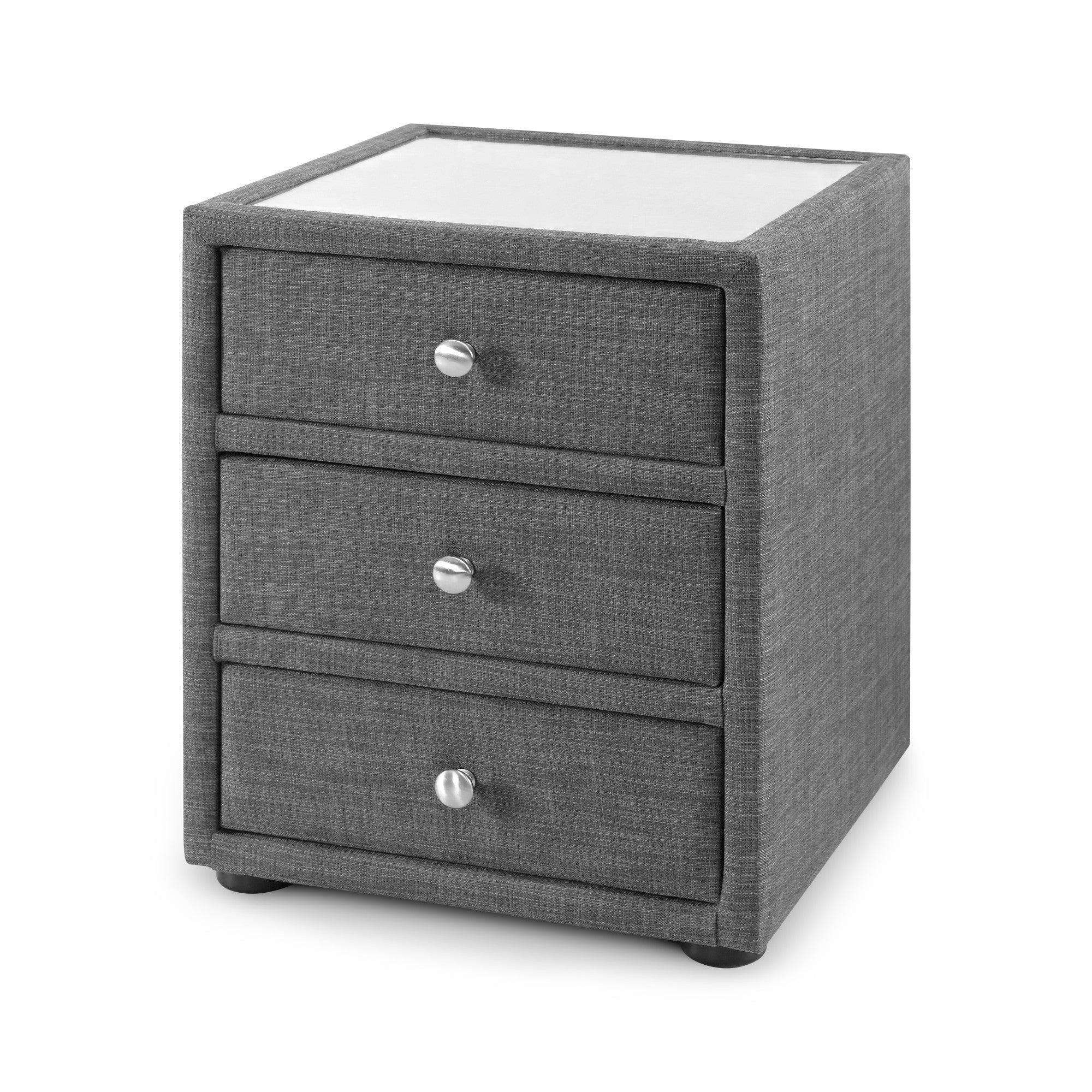 Grey fabric bedside table with three drawers and chrome handles, shown at an angle