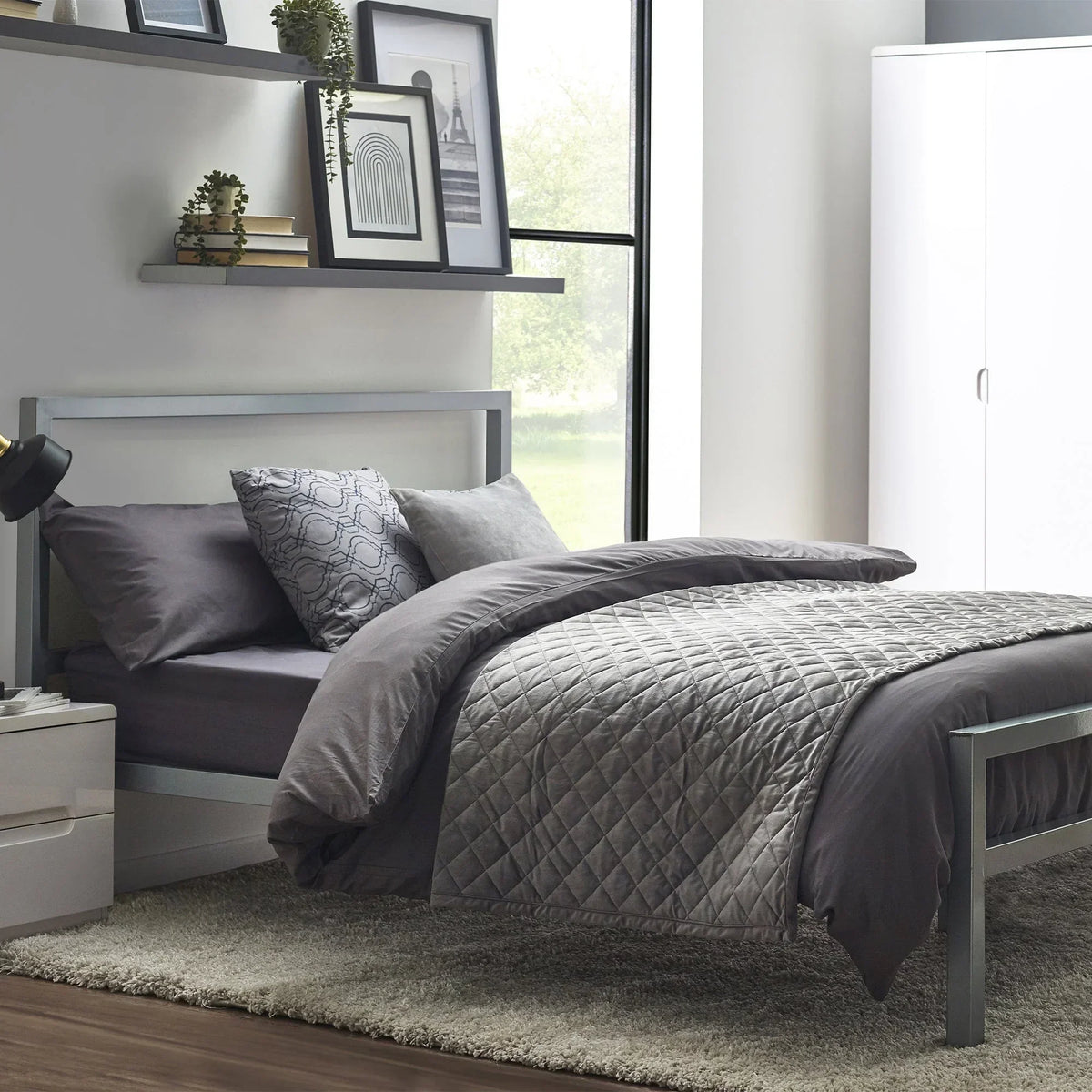Grey metal bed frame with headboard, quilted bedding and pillows in modern bedroom