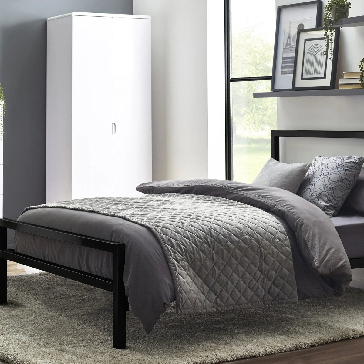 Black metal bed with grey quilted bedding in modern bedroom with wardrobe and artwork