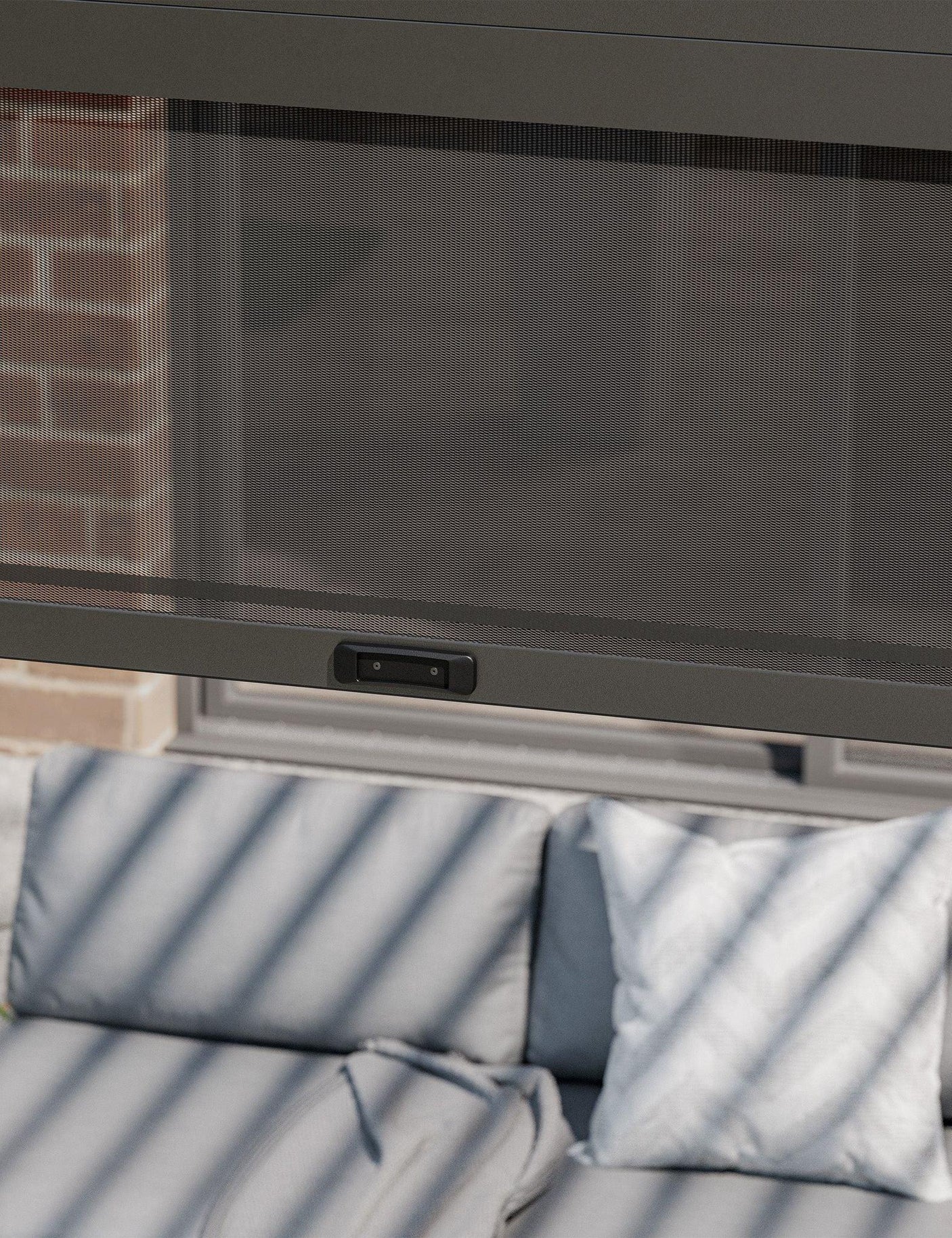 Outdoor sofa with grey cushions under a retractable mesh screen on patio