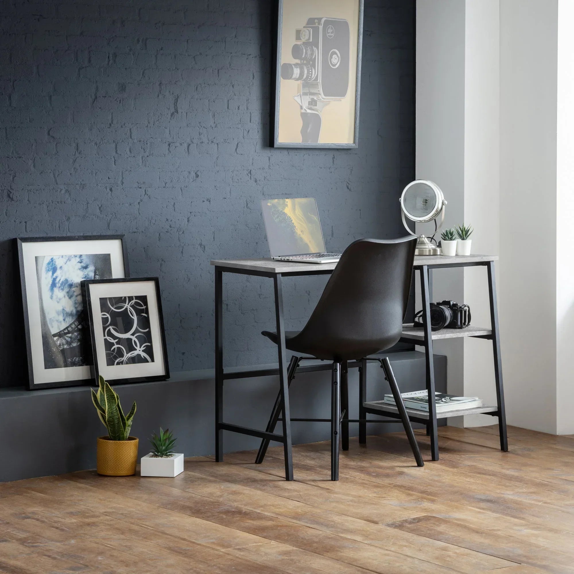 Black desk and chair set with shelves in modern home office, laptop and framed prints