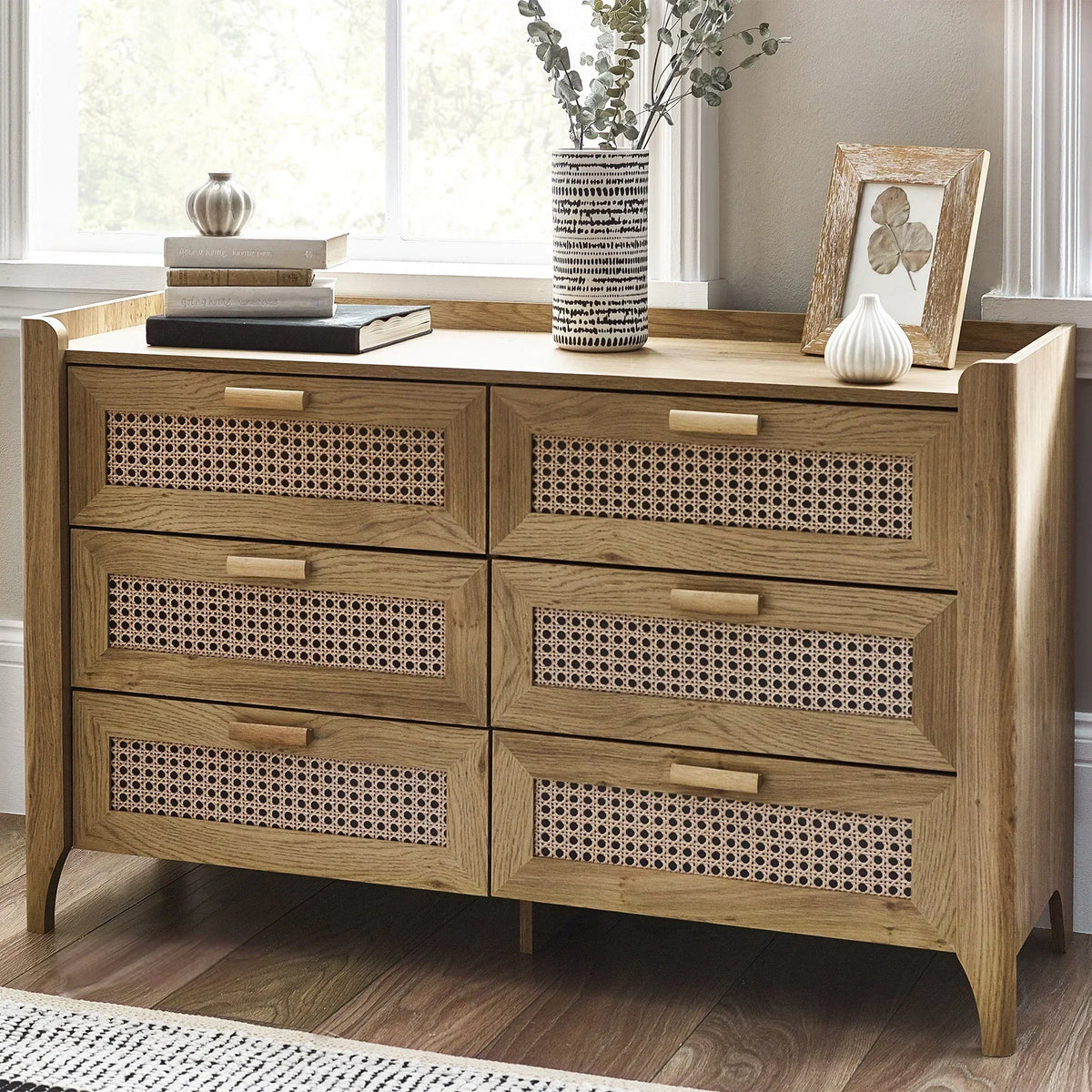 Wide rattan effect 6 drawer chest in natural wood finish beside window, decorated with vases