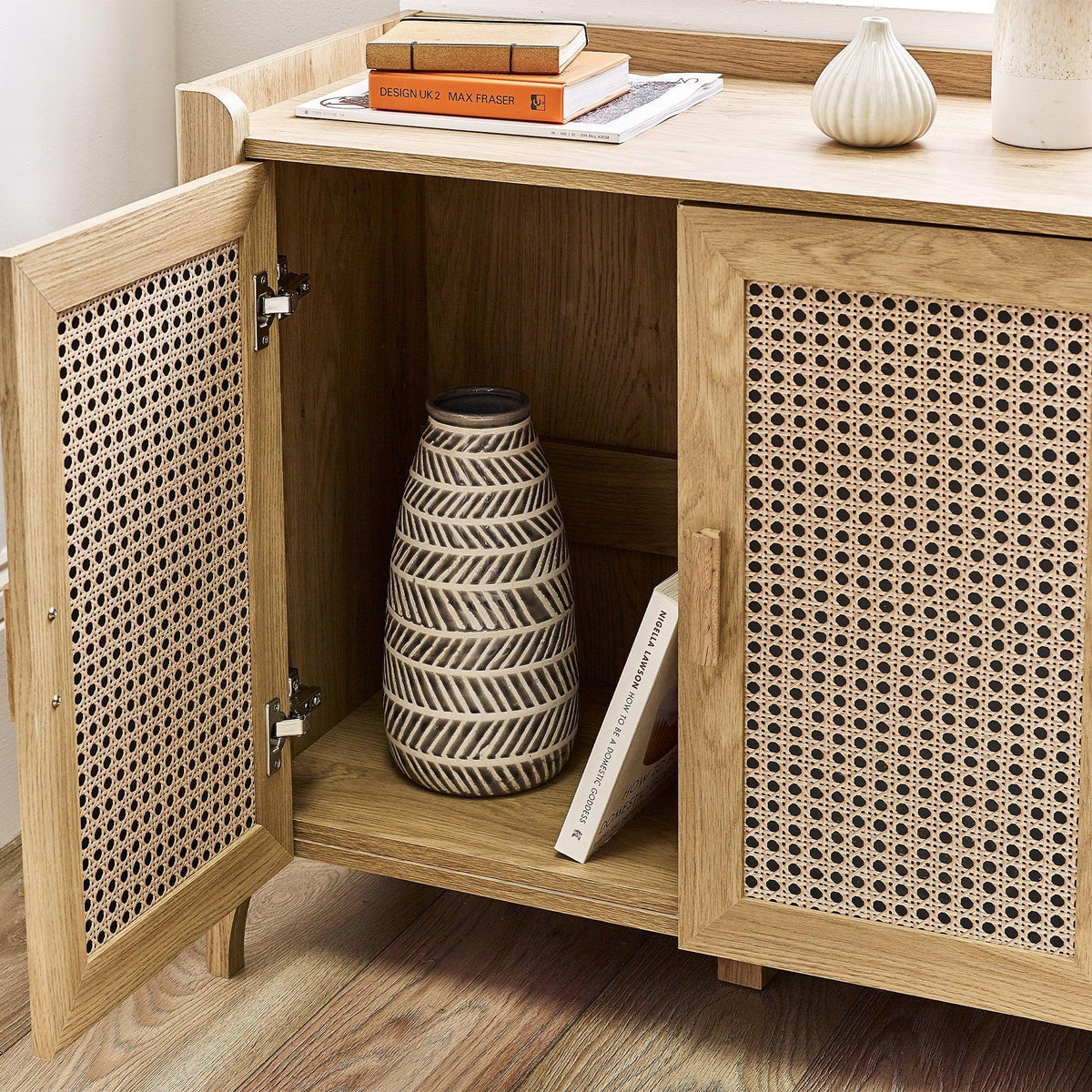 Rattan sideboard with open door showing storage shelf, ceramic vase, and wooden surface