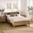 Oak wood bed with built-in shelves in headboard, beige bedding, side tables and botanical decor in room