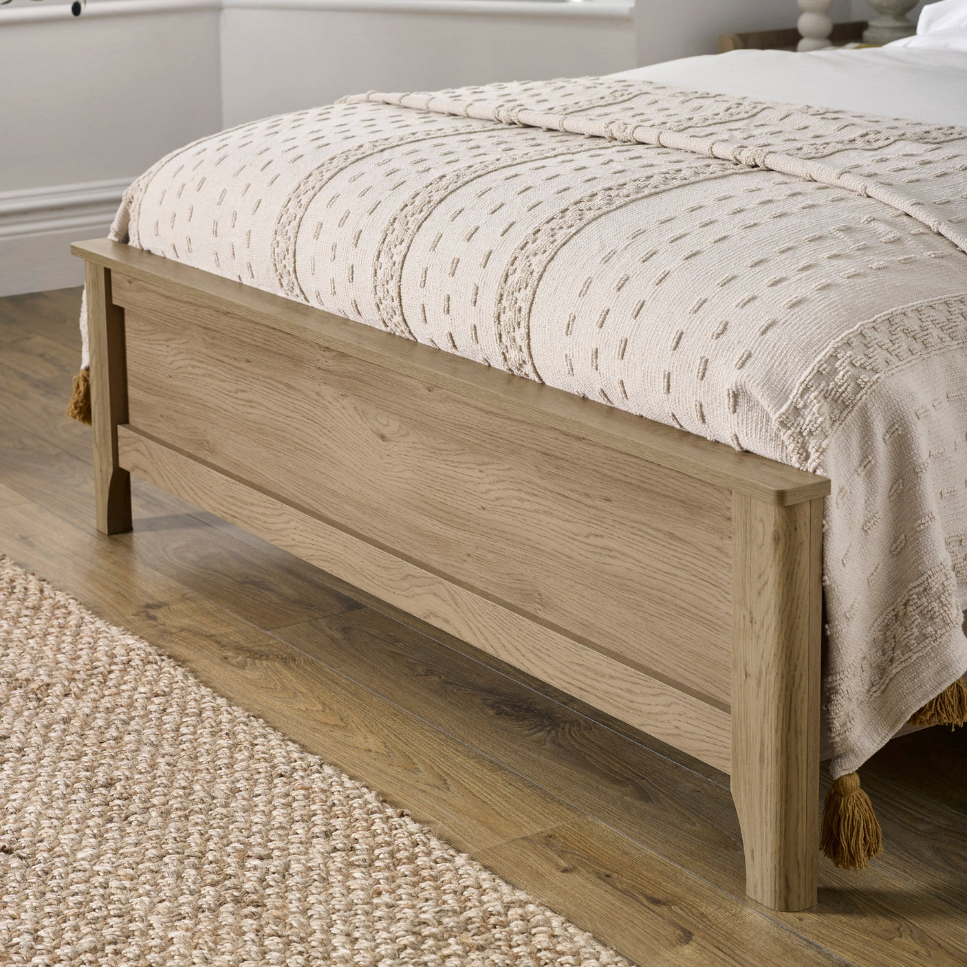 Close-up of oak wood footboard with beige textured blanket and wooden floor