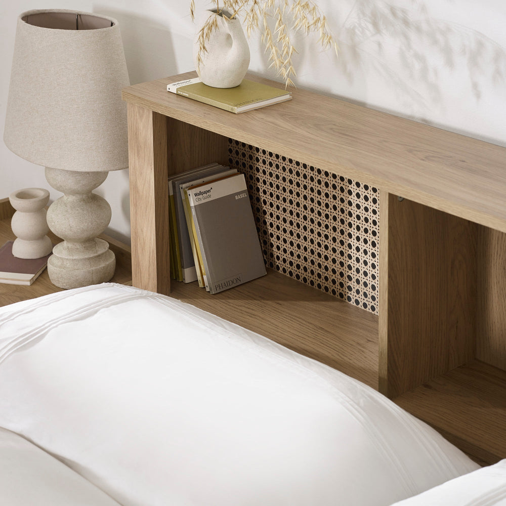 Close-up of oak headboard shelving with books, lamp and decorative vase on top