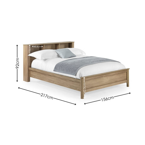 Natural wood double bed with rattan inset storage shelves in headboard, white bedding and grey throw, angled view