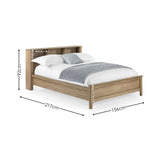 Natural wood double bed with rattan inset storage shelves in headboard, white bedding and grey throw, angled view