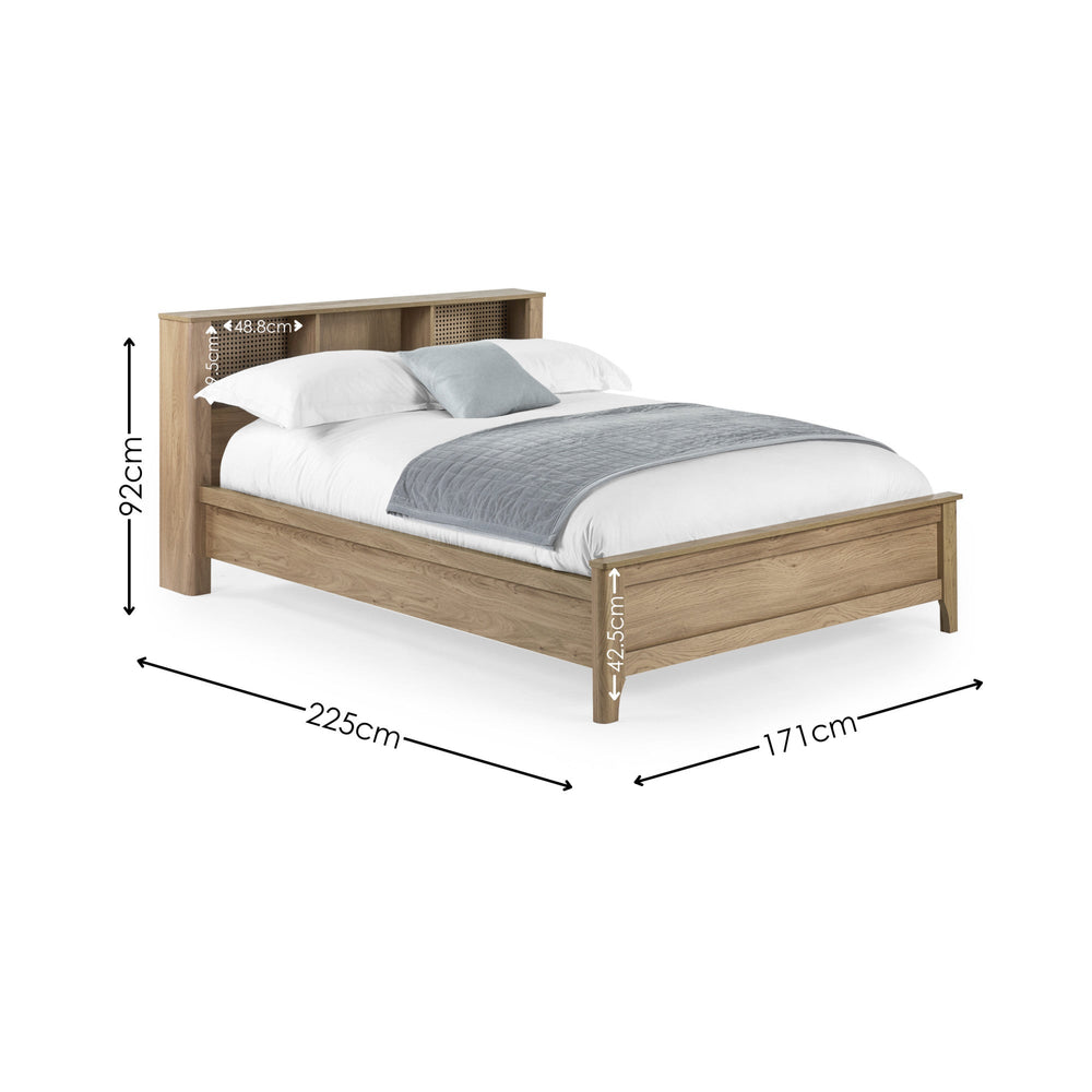 Oak wood king double bed with rattan inset storage shelves in headboard, white bedding and grey throw, angled view