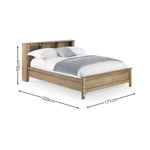 Oak wood king double bed with rattan inset storage shelves in headboard, white bedding and grey throw, angled view